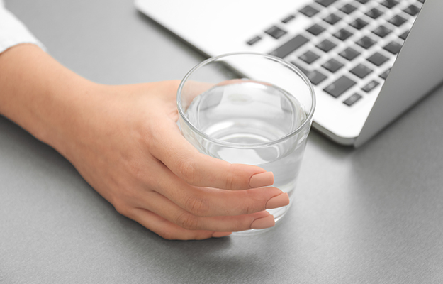 A glass of water being held next to a laptop.