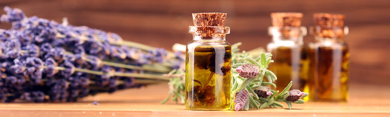 Lavender oil next to a bunch of lavender on a wooden table.
